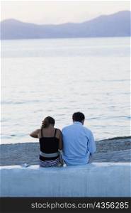 Rear view of a couple sitting on a wall near a beach, Mykonos, Cyclades Islands, Greece