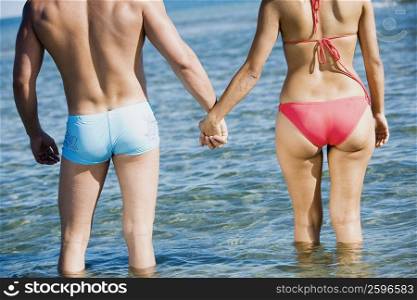Rear view of a couple standing in water and holding hands