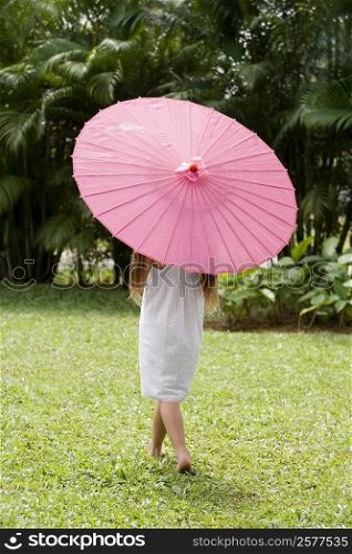 Rear view of a girl holding a parasol and walking in a park