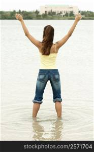 Rear view of a girl standing in water with her arms outstretched