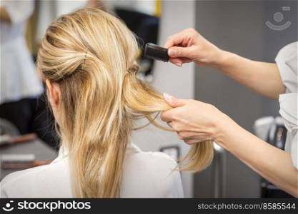 Rear View of a hairdresser combs blonde hair of the young woman in a beauty salon. Hairdresser combs hair of woman
