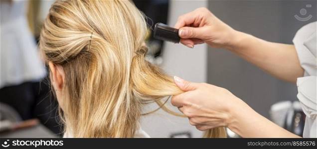 Rear View of a hairdresser combs blonde hair of the young woman in a beauty salon. Hairdresser combs hair of woman