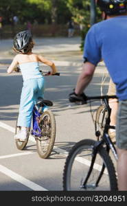 Rear view of a man and a girl cycling