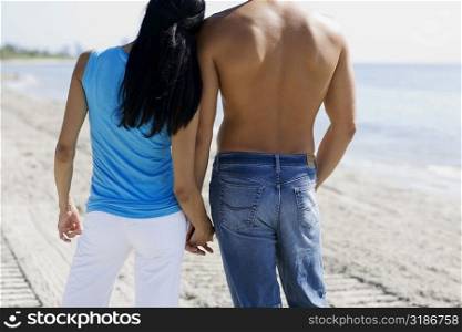 Rear view of a man and a woman holding hands on the beach