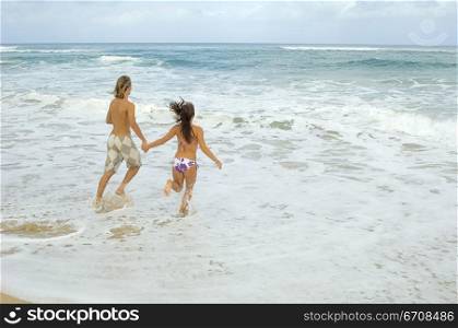 Rear view of a man and a woman running on the beach