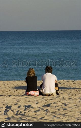 Rear view of a man and a woman sitting on the beach, South Beach, Miami, Florida, USA