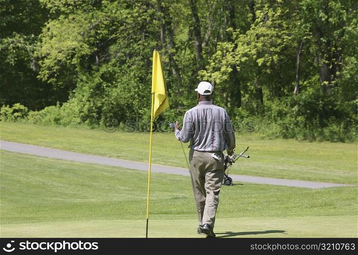 Rear view of a man carrying a golf club on a golf course