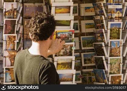 Rear view of a man choosing postcards, Piazza Della Cisterna, San Gimignano, Siena Province, Tuscany, Italy