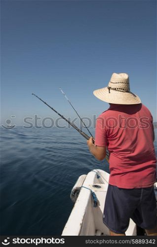 Rear view of a man fishing on boat in sea, Ixtapa, Zihuatanejo, Guerrero, Mexico