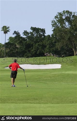Rear view of a man holding a golf club and standing in a golf course