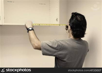Rear view of a man measuring a wooden board with a tape measure