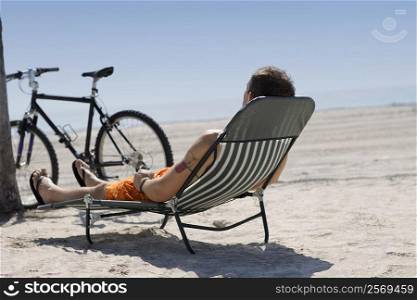 Rear view of a man reclining on a lounge chair on the beach