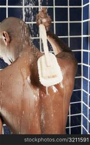 Rear view of a man scrubbing his back with a back brush