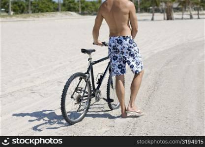 Rear view of a man standing and holding a bicycle on the beach