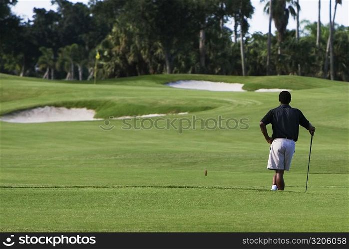 Rear view of a man standing with a golf club in a golf course