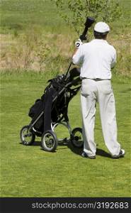 Rear view of a man taking out a golf club from a golf bag