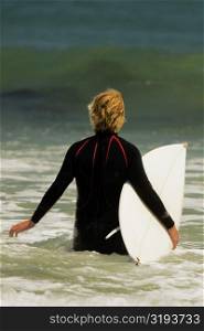 Rear view of a man walking into the sea with a surfboard