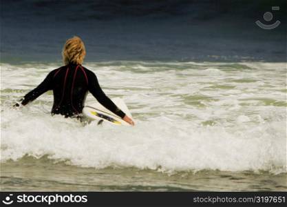 Rear view of a man walking into the sea with a surfboard