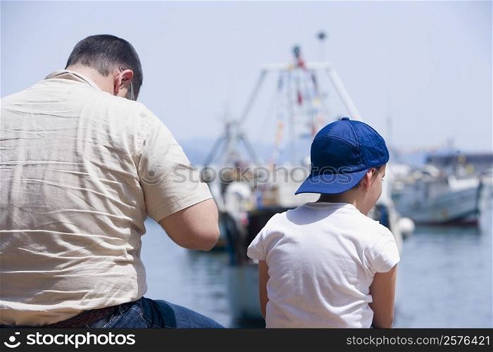 Rear view of a man with a boy sitting at the seaside, Italian Riviera, Santa Margherita Ligure, Genoa, Liguria, Italy