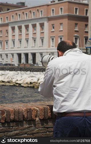 Rear view of a man with a hand-held telescope, Via Partenope, Bay of Naples, Naples, Naples Province, Campania, Italy
