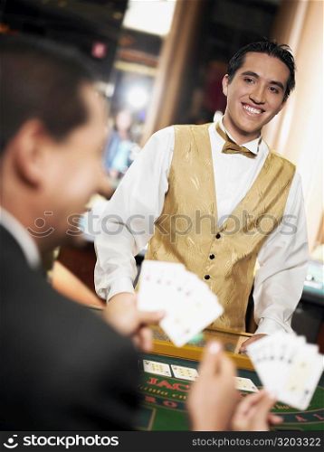 Rear view of a mature man holding playing cards with a casino worker standing in front of him