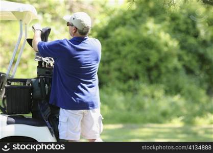 Rear view of a mature man picking a golf club from a golf bag