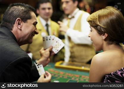 Rear view of a mature man showing playing cards to a young woman in a casino