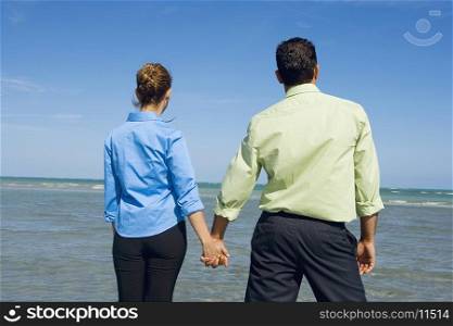 Rear view of a mid adult couple standing on the beach and holding hands