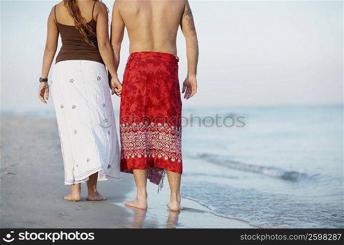 Rear view of a mid adult man and a young woman holding hands on the beach