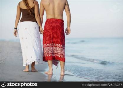 Rear view of a mid adult man and a young woman holding hands on the beach