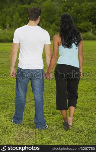 Rear view of a mid adult man and a young woman holding hands and walking