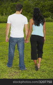 Rear view of a mid adult man and a young woman holding hands and walking