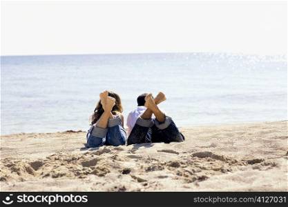 Rear view of a mid adult man and a young woman lying on the beach