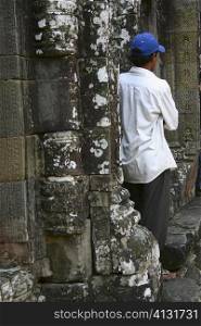Rear view of a mid adult man leaning against a wall, Ta Prohm Temple, Angkor Wat, Siem Reap, Cambodia