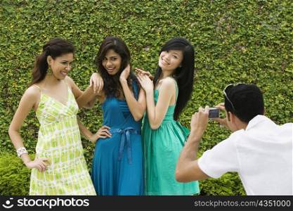 Rear view of a mid adult man photographing three young women with a digital camera