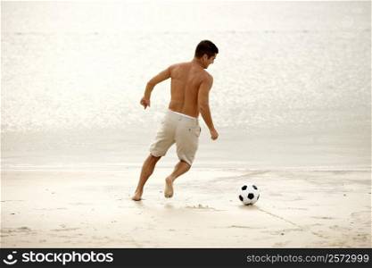 Rear view of a mid adult man playing soccer on the beach