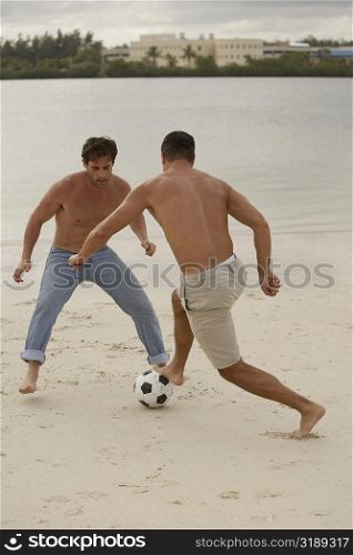 Rear view of a mid adult man playing soccer with a young man on the beach