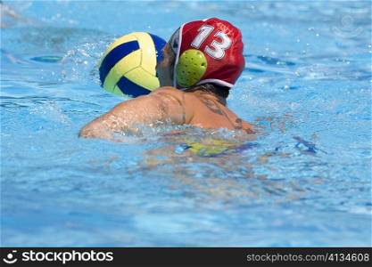 Rear view of a mid adult man playing water polo in a swimming pool