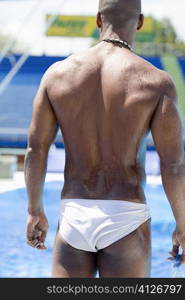 Rear view of a mid adult man standing at the poolside and holding swimming goggles