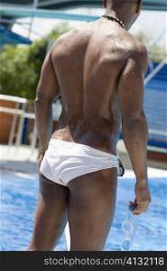 Rear view of a mid adult man standing at the poolside and holding swimming goggles