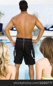 Rear view of a mid adult man standing in front of two young women at the poolside