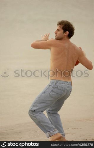 Rear view of a mid adult man throwing a rugby ball on the beach