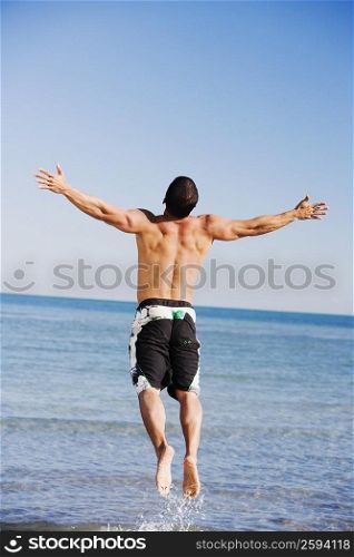 Rear view of a mid adult man with his arms outstretched jumping on the beach