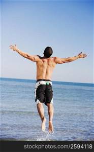 Rear view of a mid adult man with his arms outstretched jumping on the beach