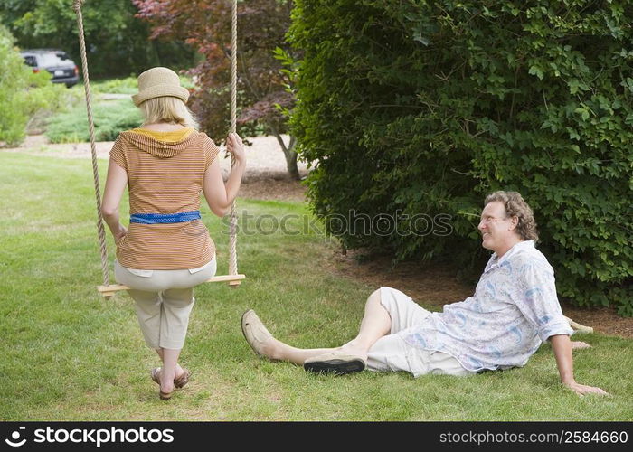 Rear view of a mid adult woman swinging on a rope swing with a mature man looking at him in a park