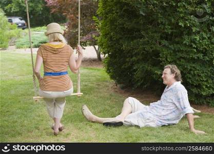 Rear view of a mid adult woman swinging on a rope swing with a mature man looking at him in a park