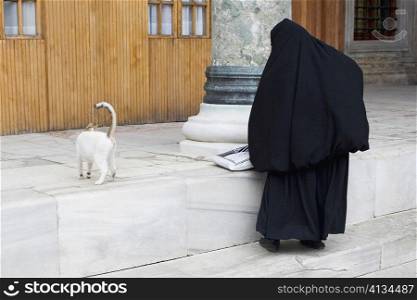 Rear view of a Muslim woman in hijab standing with a cat, Istanbul, Turkey