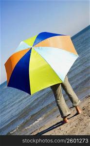 Rear view of a person with an umbrella standing on the beach