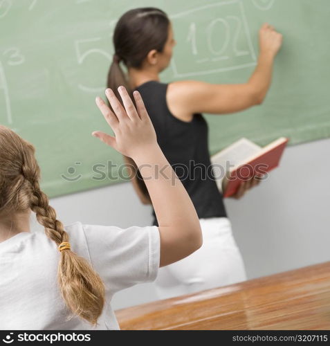 Rear view of a schoolgirl in a classroom with her hand raised
