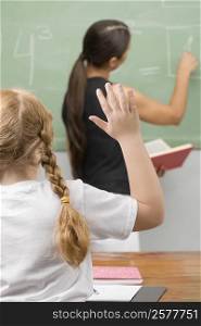 Rear view of a schoolgirl with her hand raised in a classroom